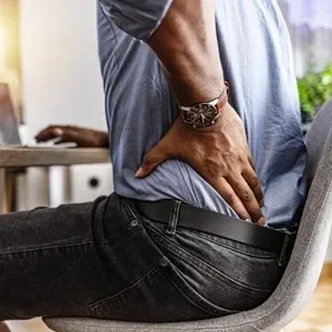 A man in an office chair holding his lower back in pain
