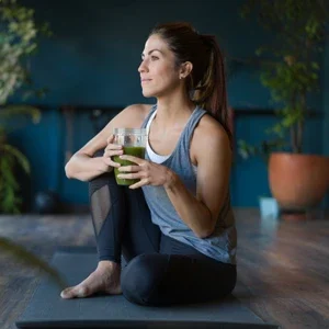 A woman wearing fitness clothing and drinking a green smoothie